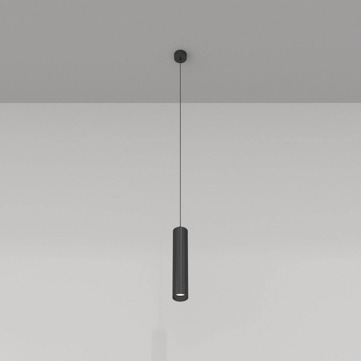 The Focus Single Pendant Light - Black hangs gracefully from the ceiling with its black metal finish, casting light downward. It highlights a modern industrial aesthetic against the smooth white wall, emphasizing simplicity and elegance in design.