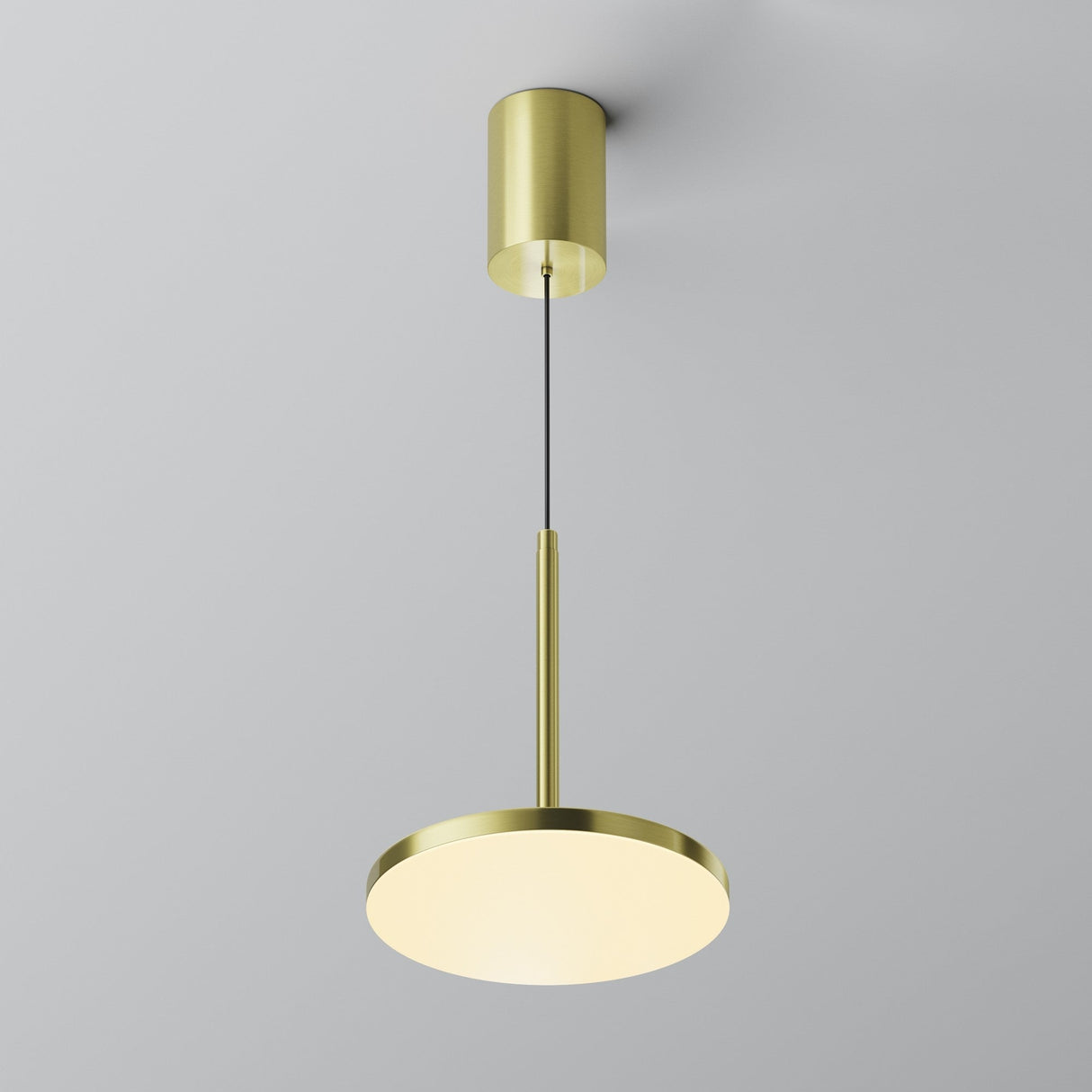 The Plato LED Pendant Light - Brass features a sleek, cylinder mount and slim stem with a flat round diffuser, elegantly illuminated against a plain light gray background.