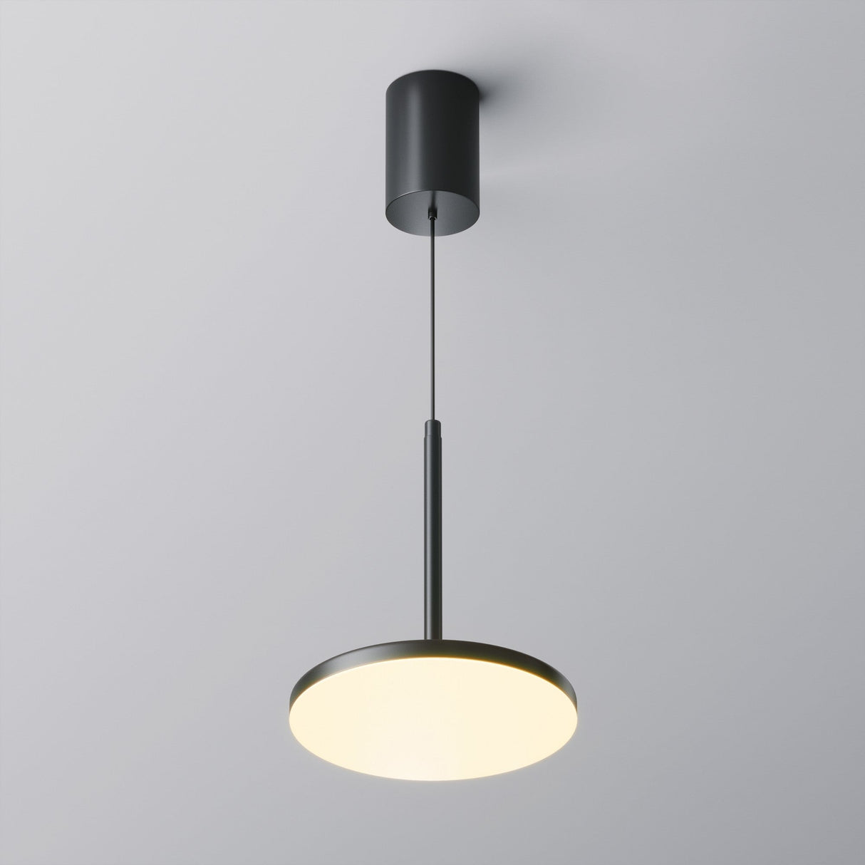 The Plato LED Pendant Light - Black is a modern, minimalist fixture with energy-efficient LED technology. It features a black cylindrical design and thin cord suspending a round illuminated disc, perfect for enhancing modern interiors with sleek design and soft illumination against a white ceiling.
