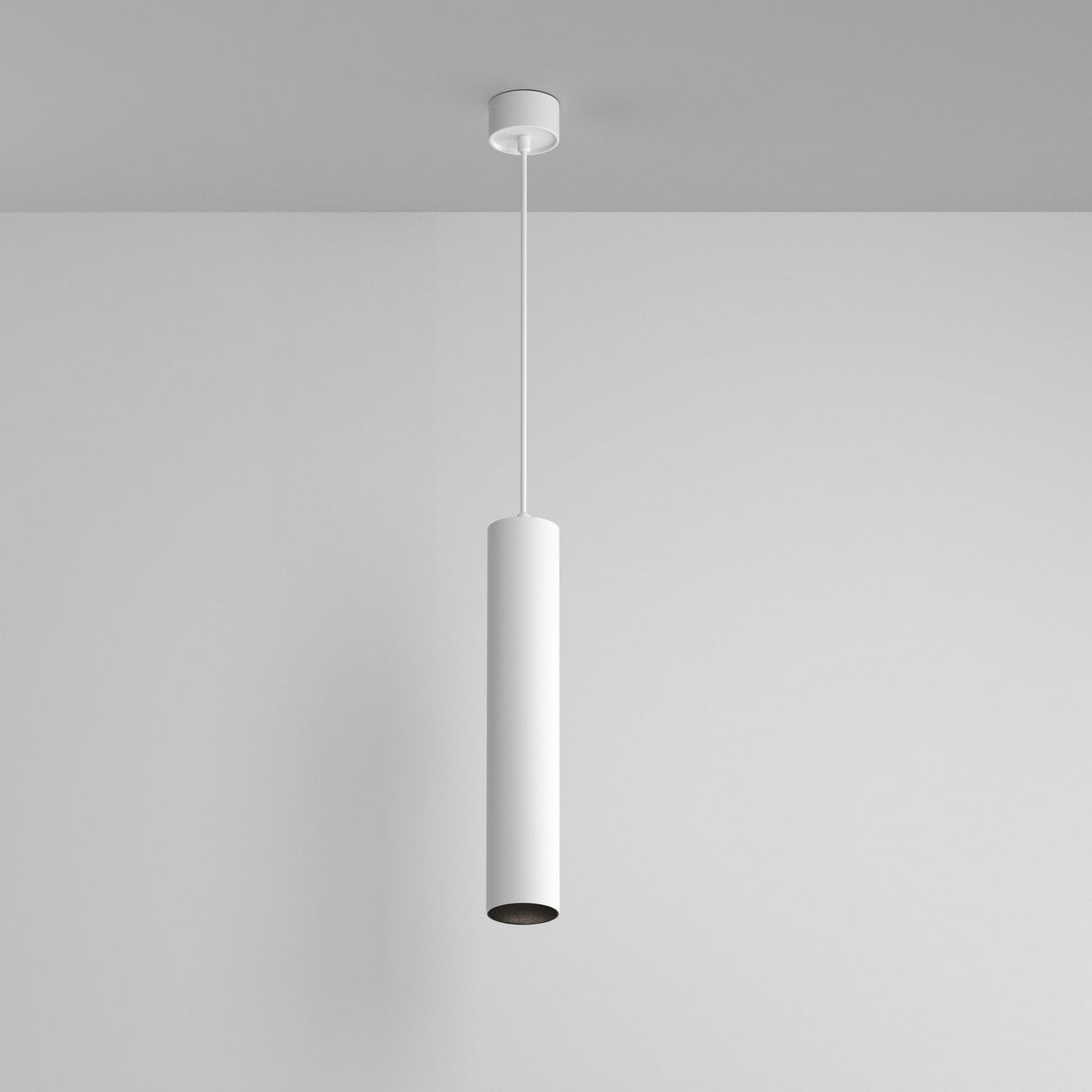 The Artisan 1 Light Long Round Pendant, featuring a sleek white finish and minimalist cylindrical design, hangs elegantly from the ceiling against a plain wall, embodying modern lighting design.