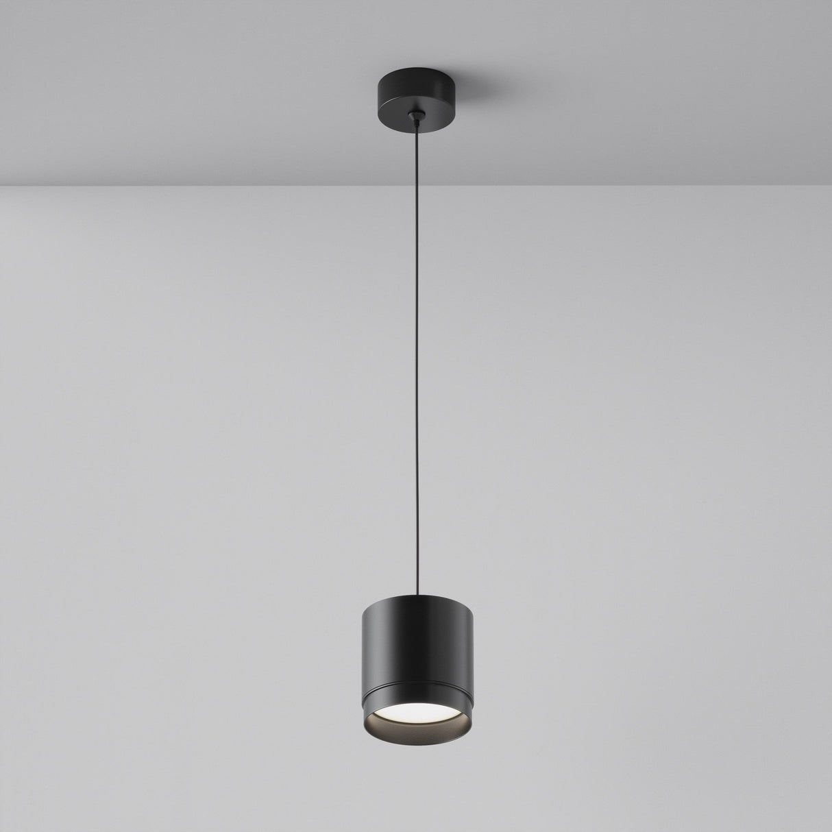 The Polar Short Round Pendant Light - Black, with a contemporary design and matte black finish, elegantly hangs from a gray ceiling. Its slender cord gracefully suspends the light, softly illuminating the surface below.