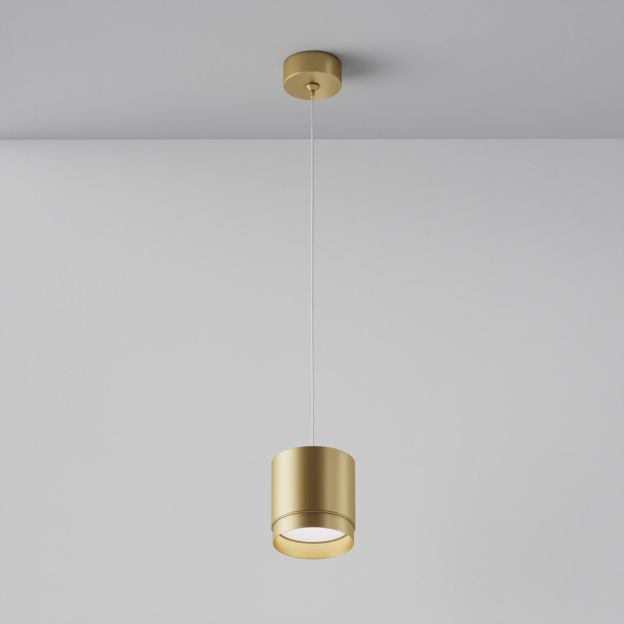 The Polar Short Round Pendant Light - Matte Gold features a cylindrical shade and a thin wire, hanging against a plain grey background. The interior lighting fixture emits a soft downward glow.