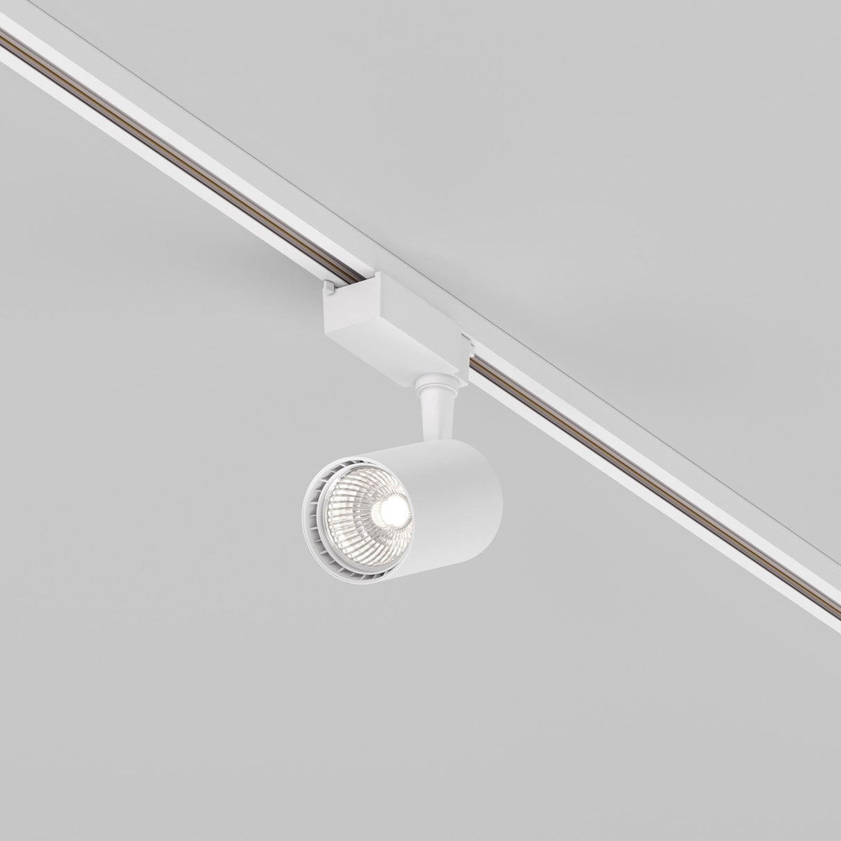 The Vuoro S LED Single Phase Unity Track Spotlight (10W, 4000K) in modern white is mounted on the ceiling. Its cylindrical lamp features a swivel mechanism that directs light downward, revealing a visible lit bulb and giving the light gray area a minimalist appearance.