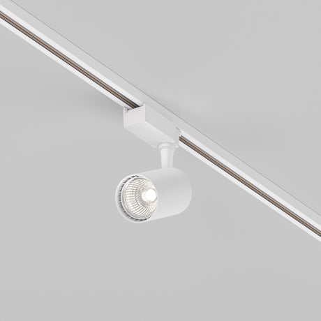 The Vuoro S LED Single Phase Unity Track Spotlight (10W, 4000K) in modern white is mounted on the ceiling. Its cylindrical lamp features a swivel mechanism that directs light downward, revealing a visible lit bulb and giving the light gray area a minimalist appearance.