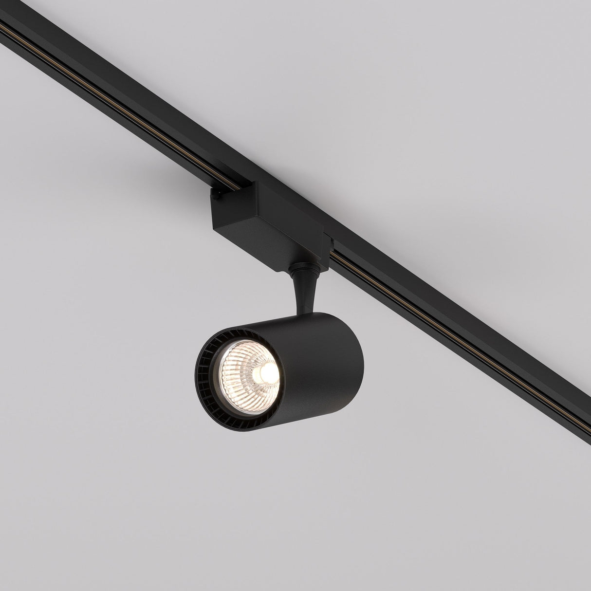 The Vuoro S LED 15W Track Spotlight in black features a modern cylindrical design on a ceiling rail, with an adjustable swivel mechanism that contrasts against the light gray background, illuminating the section below with its 3000K single-phase light.
