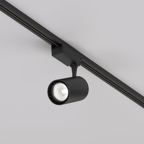 The Vuoro S LED Single Phase Unity Track Spotlight 15W 4000K in black is a minimalist cylindrical fixture mounted on the ceiling, angled downward. It emits bright 4000K light with energy efficiency, seamlessly blending in with any decor without sacrificing style.