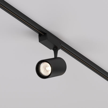 The Vuoro S LED Single Phase Unity Track Spotlight 26W 3000K in black is sleek and cylindrical, mounted to a ceiling rail and angled downward. It casts a bright, energy-efficient glow that stands out against the light gray ceiling, enhancing the ambient lighting beautifully.