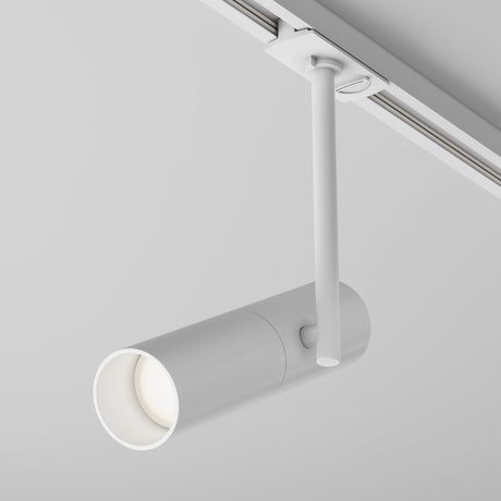 The Elti Single Phase Unity Track Spotlight in white, with a cylindrical shape and minimalist design, mounts on a ceiling track for adjustable lighting. It features a tubular form and simple arm against a plain light gray backdrop.