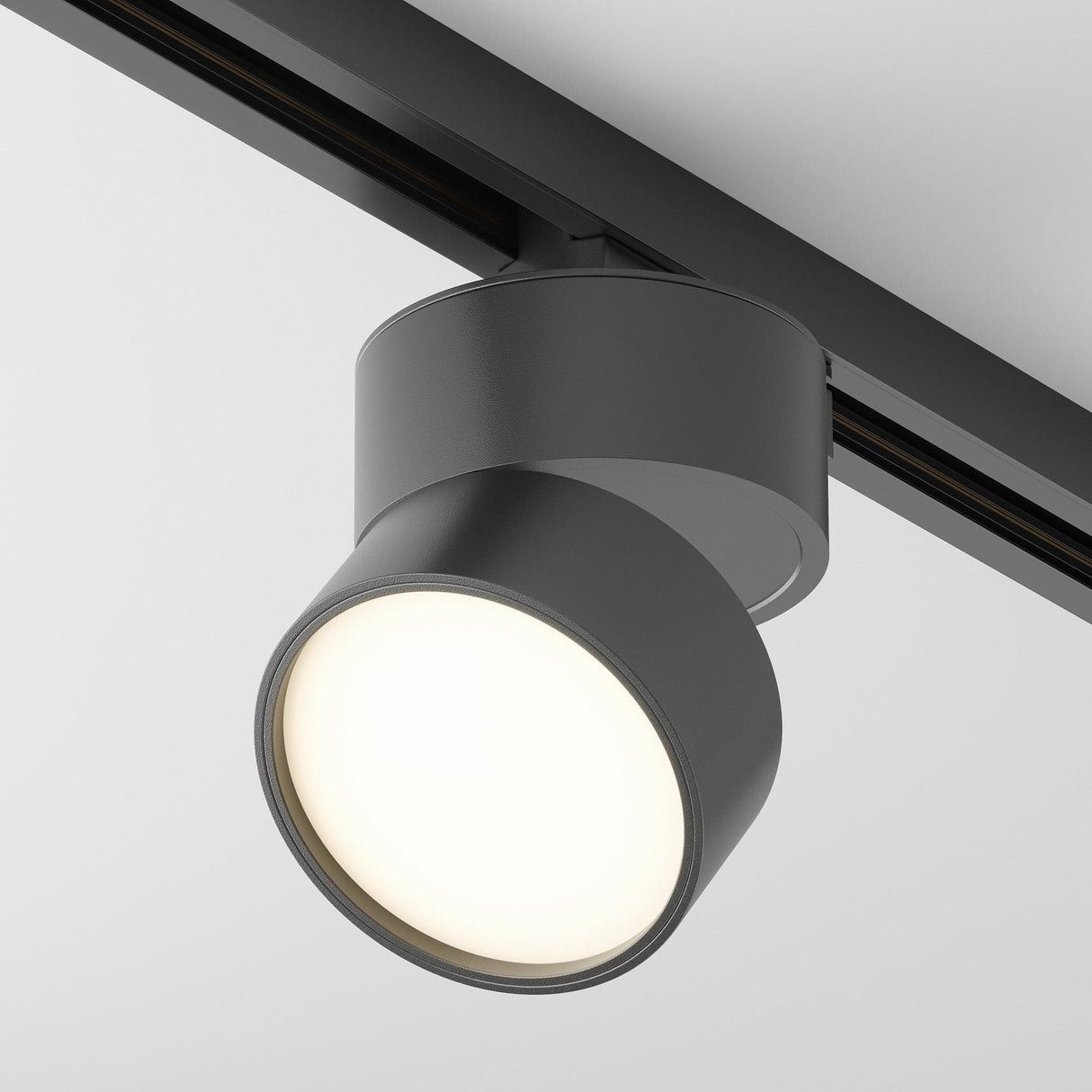 The Onda LED Single Phase Unity Track Spotlight 12W 3000K - Black, with its cylindrical design, is mounted on a ceiling track. Its sleek, minimalist style enhances modern interiors by casting a bright glow from its smooth, rounded face.