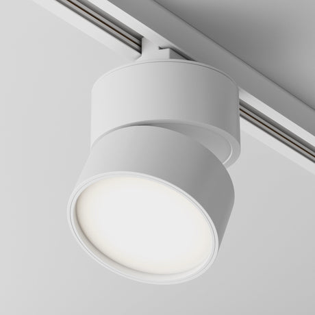 The Onda LED Single Phase Unity Track Spotlight 12W 3000K in white features a cylindrical design with an LED spotlight that casts a warm glow, complete with an anti-glare grille and sleek, minimalist look for contemporary lighting on gray surfaces.