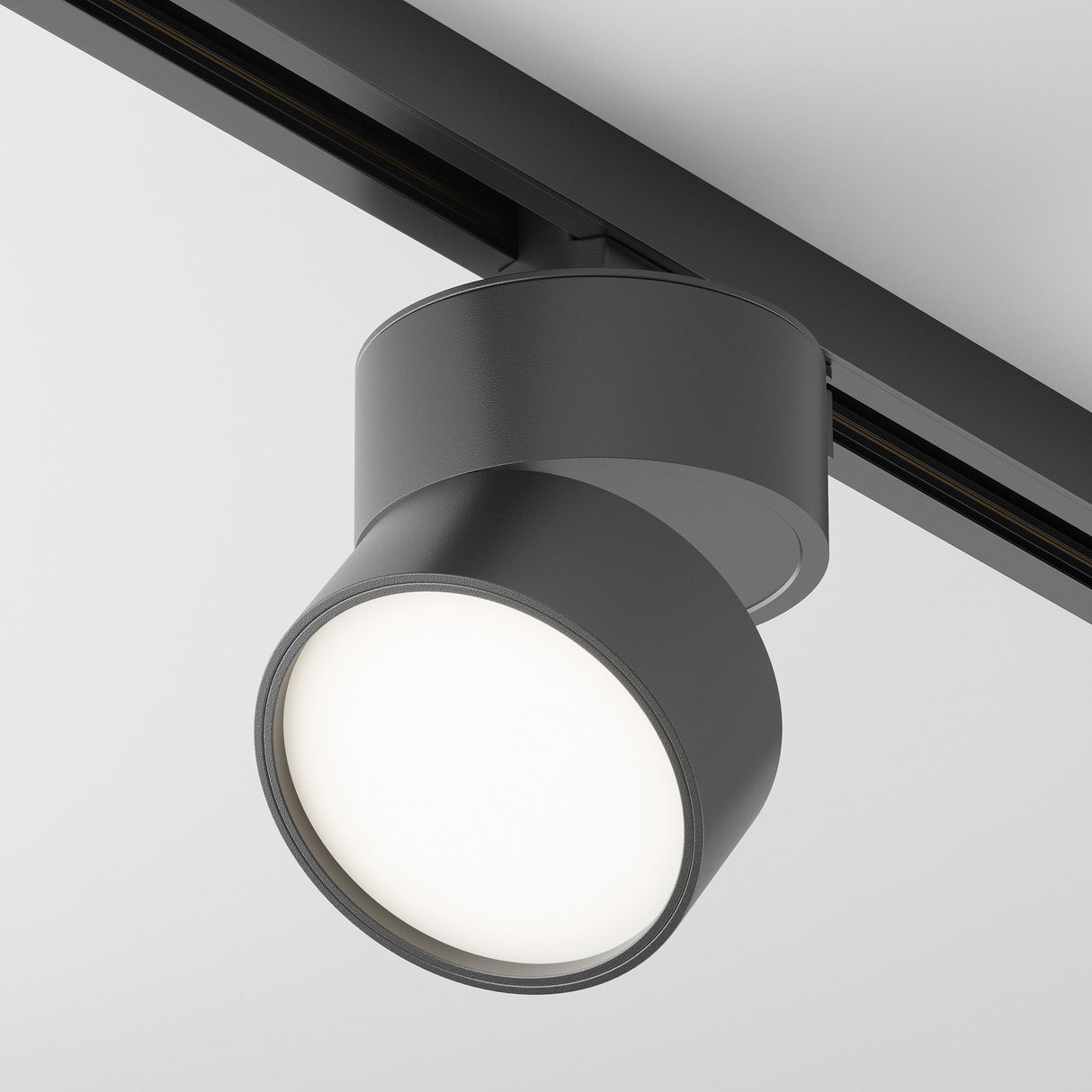 The Onda LED Single Phase Unity Track Spotlight 12W 4000K in black is mounted on a ceiling rail, offering modern cylindrical design that emits bright white light, perfectly enhancing contemporary interiors against a plain white ceiling.