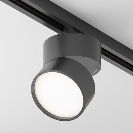 The Onda LED Single Phase Unity Track Spotlight 12W 4000K in black is mounted on a ceiling rail, offering modern cylindrical design that emits bright white light, perfectly enhancing contemporary interiors against a plain white ceiling.