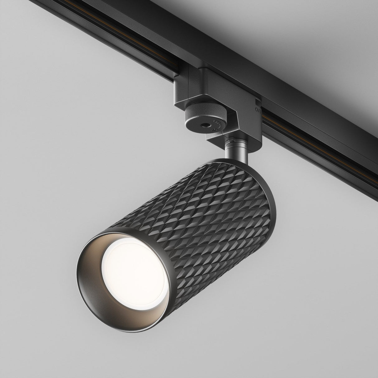 Close-up of the Focus Design Single Phase Unity Track Spotlight in black, showcasing its sleek cylindrical design on a ceiling track. The GU10 base emits a bright glow, elegantly illuminating the room.