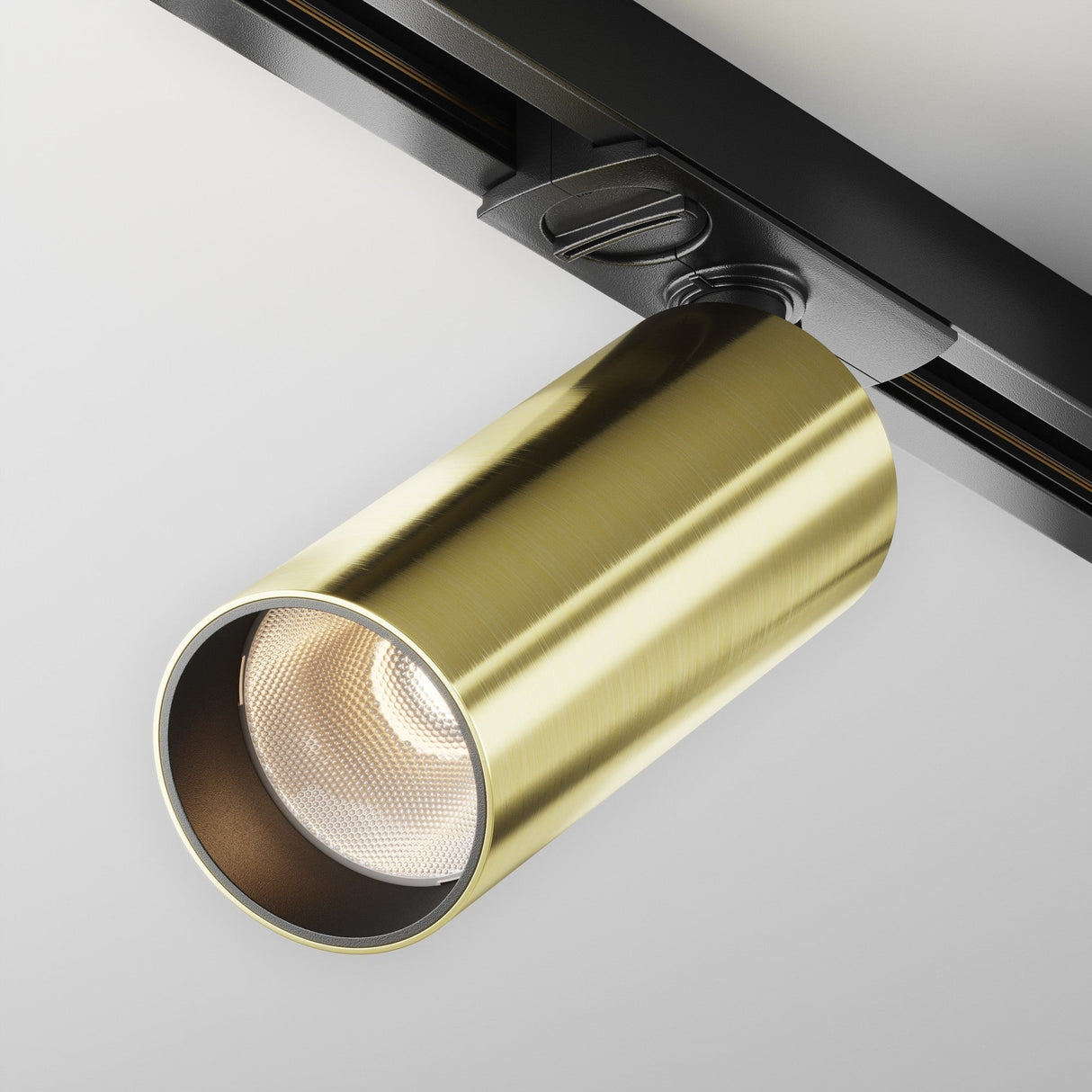 A close-up of the Focus LED Single Phase Unity Track Spotlight showcases its sleek, contemporary design with a cylindrical brushed brass finish, wide beam angle, and is attached to a black mounting bracket. .