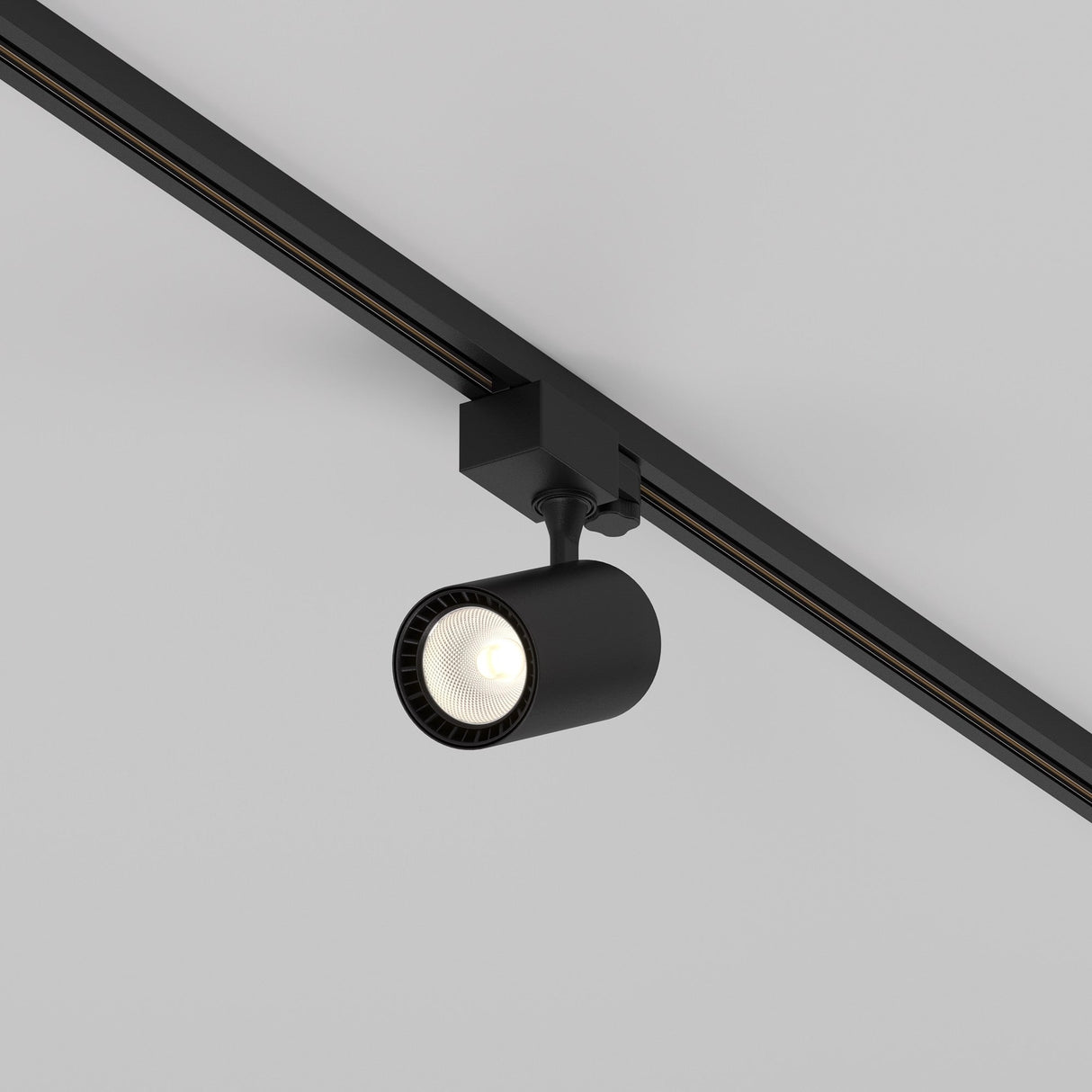 The Vuoro S 3-Circuit Trinity Track LED Spotlight 10W 3000K in black is mounted on a white ceiling. Its cylindrical head, with an adjustable swivel, points downward to illuminate the area below.