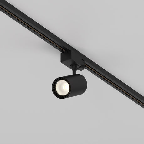The Vuoro S 3-Circuit Trinity Track LED Spotlight 10W 3000K in black is mounted on a white ceiling. Its cylindrical head, with an adjustable swivel, points downward to illuminate the area below.