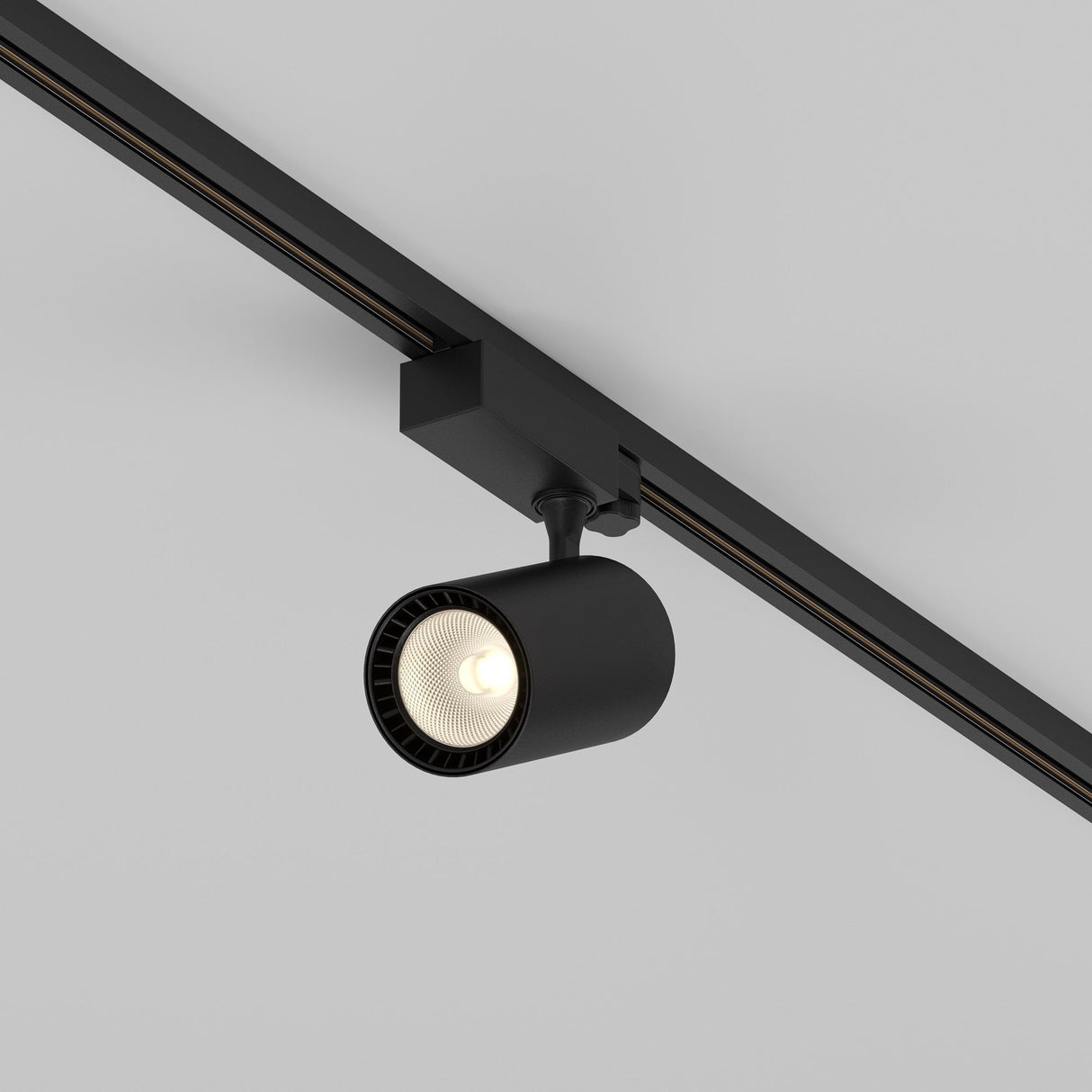 The Vuoro S 3-Circuit Trinity Track LED Spotlight 26W 3000K in black, with an adjustable swivel and cylindrical design, elegantly illuminates downward against a grey background when mounted on the ceiling.