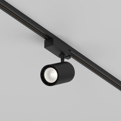 The Vuoro S 3-Circuit Trinity Track LED Spotlight 26W 4000K in black, with its cylindrical fixture and aluminum finish, is ceiling-mounted on a track, providing a sleek look and soft, focused glow to enhance the plain white ceiling for versatile lighting solutions.