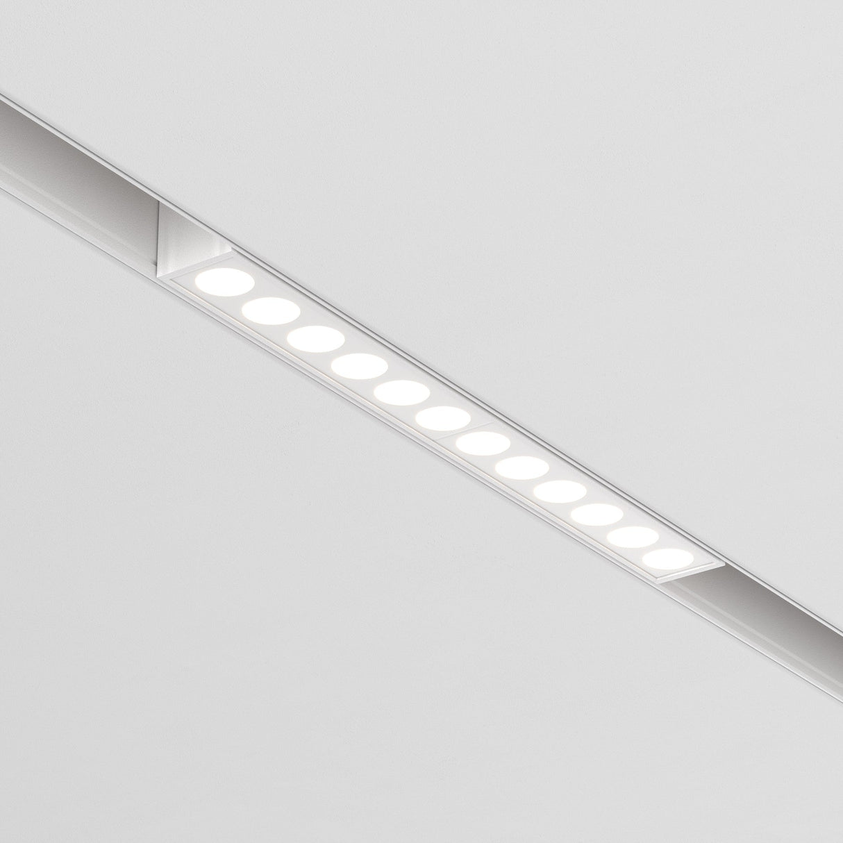 Close-up of a Points LED Linear Track Light, 12W, embedded in a white ceiling for Magnetic Exility. The fixture emits a warm 3000K glow with evenly spaced circular lights.