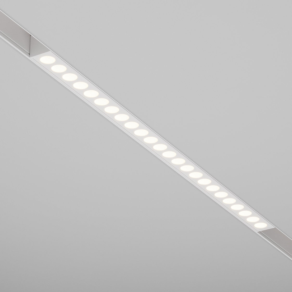 A Points DALI CCT LED Dimmable Linear Track Light, embedded in a plain light grey ceiling, provides uniform illumination with 24W power and adjustable color temperature from 2700-6000K. It emits a soft white glow with multiple evenly spaced round lights.