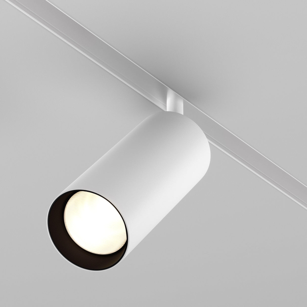 The Focus LED Magnetic Exility Track Spotlight 20W 3000K in white is mounted on a ceiling rail, illuminating downwards with energy-efficient LED technology. Its sleek design complements the minimalistic setting and enhances the plain ceiling and surroundings.
