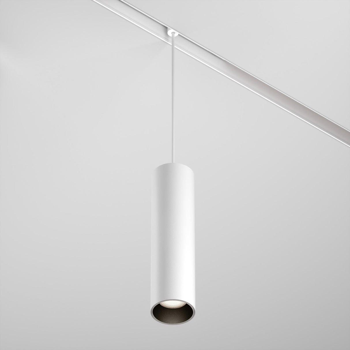 The Focus LED Exility Magnetic Track Pendant Light 12W 4000K - White, with its sleek cylindrical design, hangs elegantly from a white ceiling on a thin wire. This minimalist fixture embodies energy-efficient lighting with its clean, modern look.