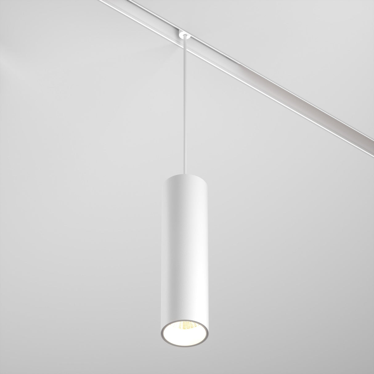 The Focus LED CCT Smart Dimmable Exility Magnetic Track Pendant Light 12W 2700-6000K in white hangs from the ceiling, emitting a soft glow. Its minimalist cylindrical design and dimmable feature complement a clean, contemporary interior space perfectly.