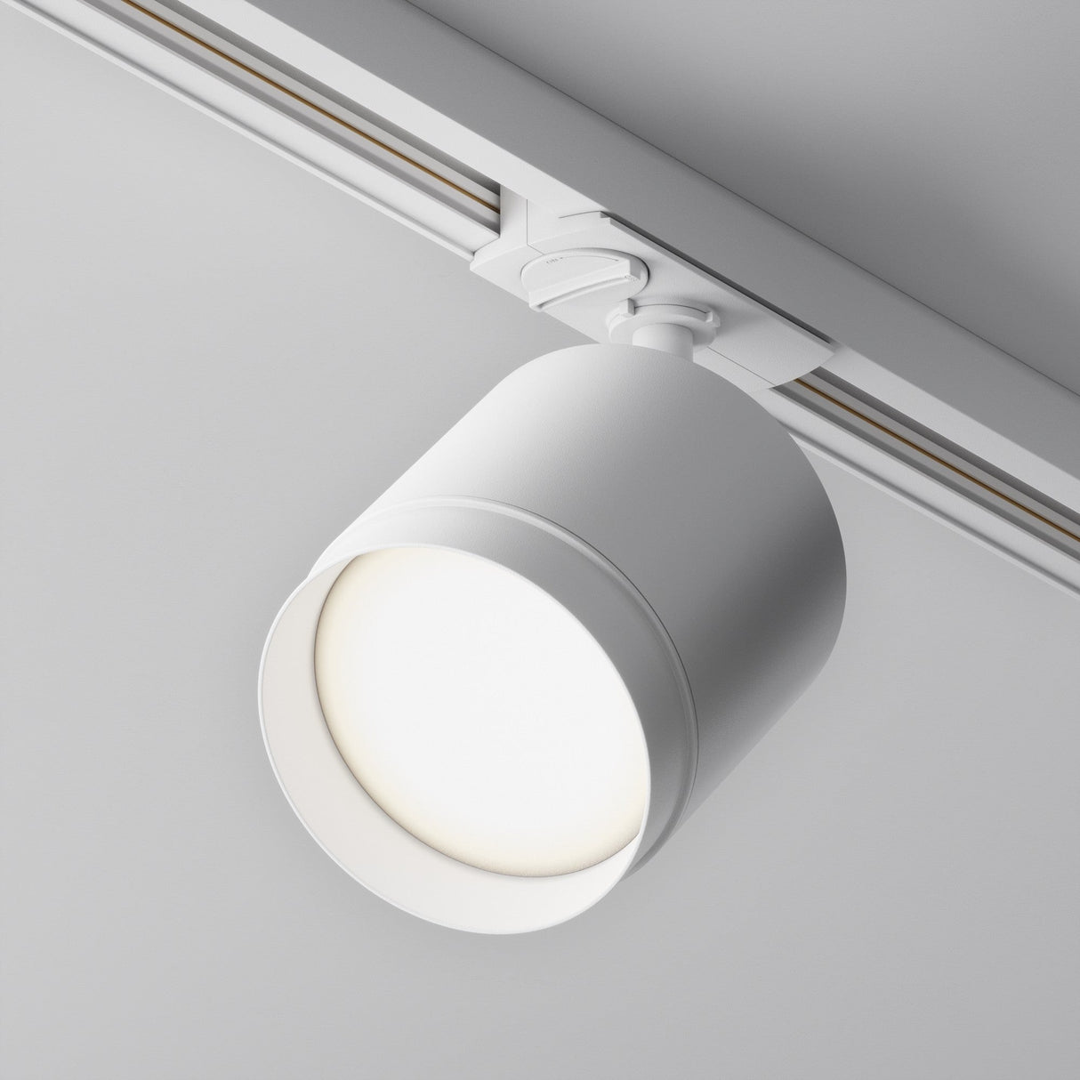 The Polar LED Single Phase Unity Track Spotlight in white is affixed to a ceiling rail, casting a bright glow against a light gray background. Ideal for modern interiors, this sleek fixture features a minimalist design and maintains a fixed position on the track.