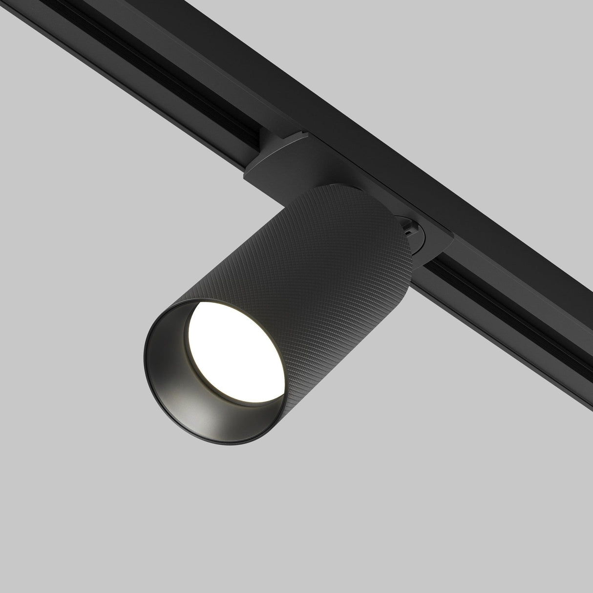 The Artisan Single Phase Unity Track Spotlight in black, with a modern cylindrical design, is installed on a ceiling rail against a light gray background. Its on, emitting an LED glow ideal for enhancing contemporary interiors.