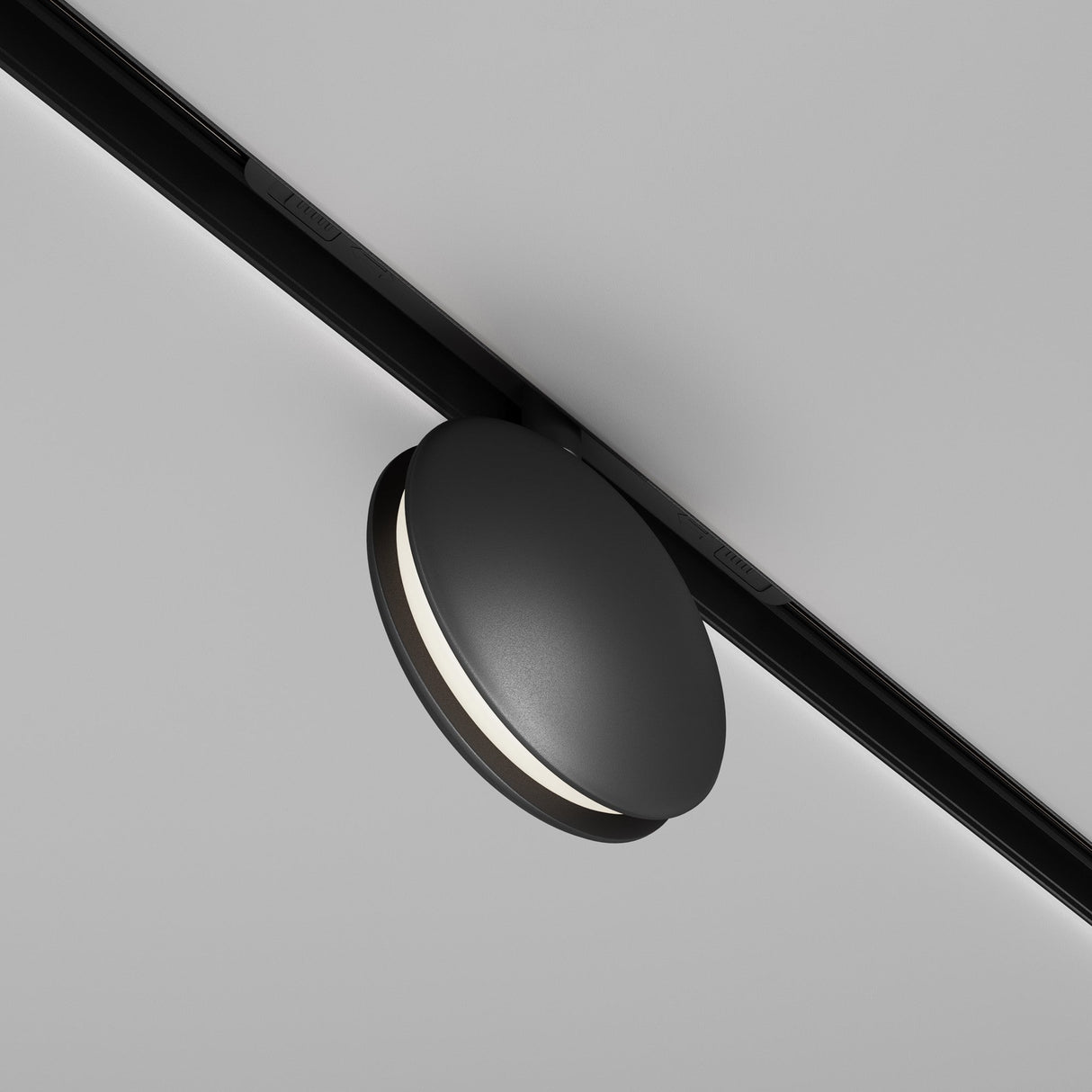 The Outline CCT LED Track Projection Light in black is a sleek, minimalist fixture with dimmable lighting (2700-6000K) and a thin line of diffused light. Its modern design features a circular 6W form attached to a white ceiling.