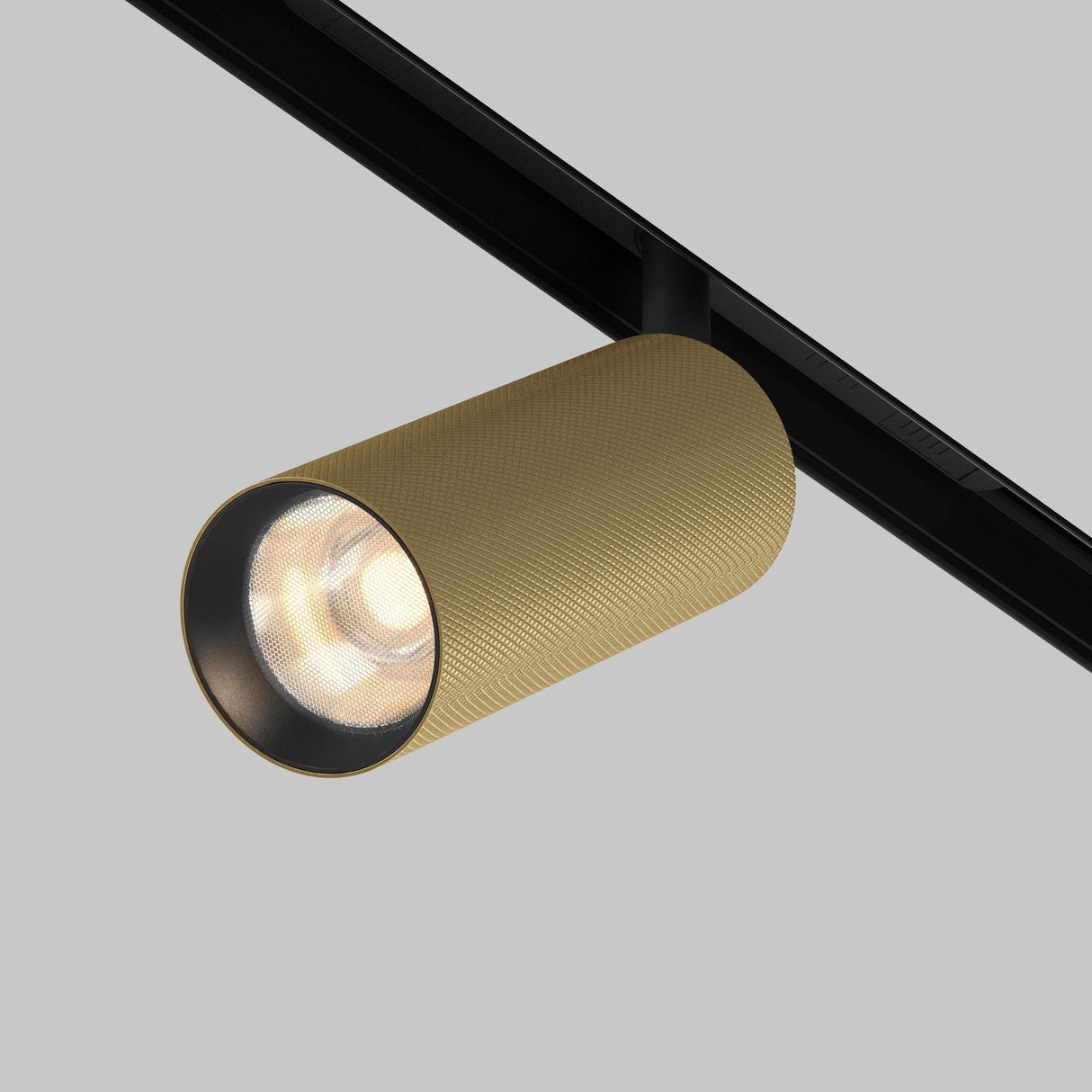 An Artisan LED Magnetic Exility Track Spotlight 12W 3000K - Black & Matte Gold with a cylindrical, diamond-textured design is mounted on a black track against a gray background. It casts bright, focused light, enhanced by the HoneyComb-D38 anti-glare filter.