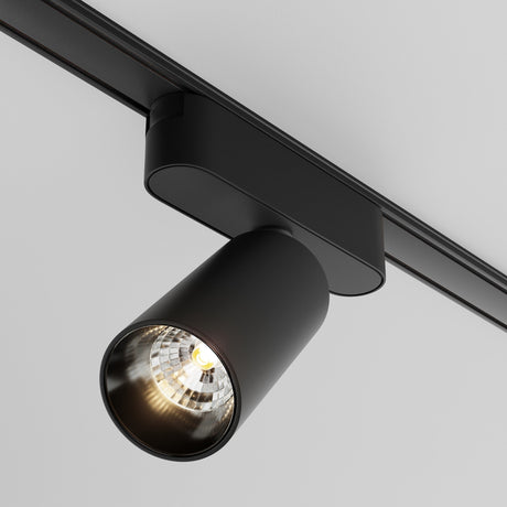 A close-up of the Focus LED Magnetic Radity Track Spotlight 12W 3000K - Black on a white ceiling, showcasing its cylindrical design and glowing bulb aimed downward. Ideal for accent lighting in modern interiors, it merges functionality with style.
