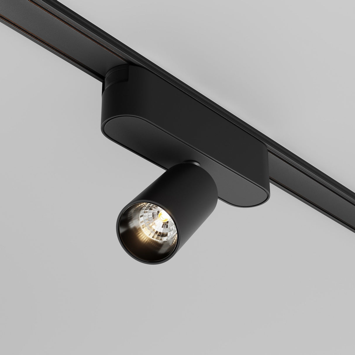 The Focus LED Magnetic Radity Track Spotlight 5W 3000K - Black features a sleek, cylindrical design and matte finish. Mounted on a ceiling rail, it casts a focused beam of accent light, complementing any neutral backdrop with its modern industrial style.