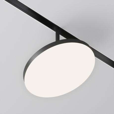 The Plato CCT LED Dimmable Magnetic Exility Track Spotlight 15W, ranging from 2700-6000K, is elegantly mounted on a black fixture. The circular white ceiling light casts a soft glow with adjustable color temperature, set against a plain white ceiling.