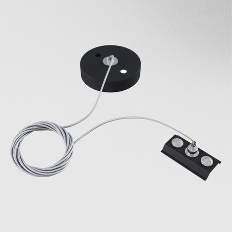 The Unity Single Phase Surface-Mounted Track Suspension Cable - Black, with its black circular base and rectangular component connected by a coiled suspension cable, evokes modern elegance against a plain white background.