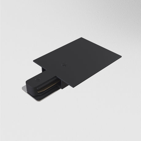 A Unity Tracks Power Feed - Black, featuring a sleek rectangular design and a protruding metal component, is mounted on a plain white wall.