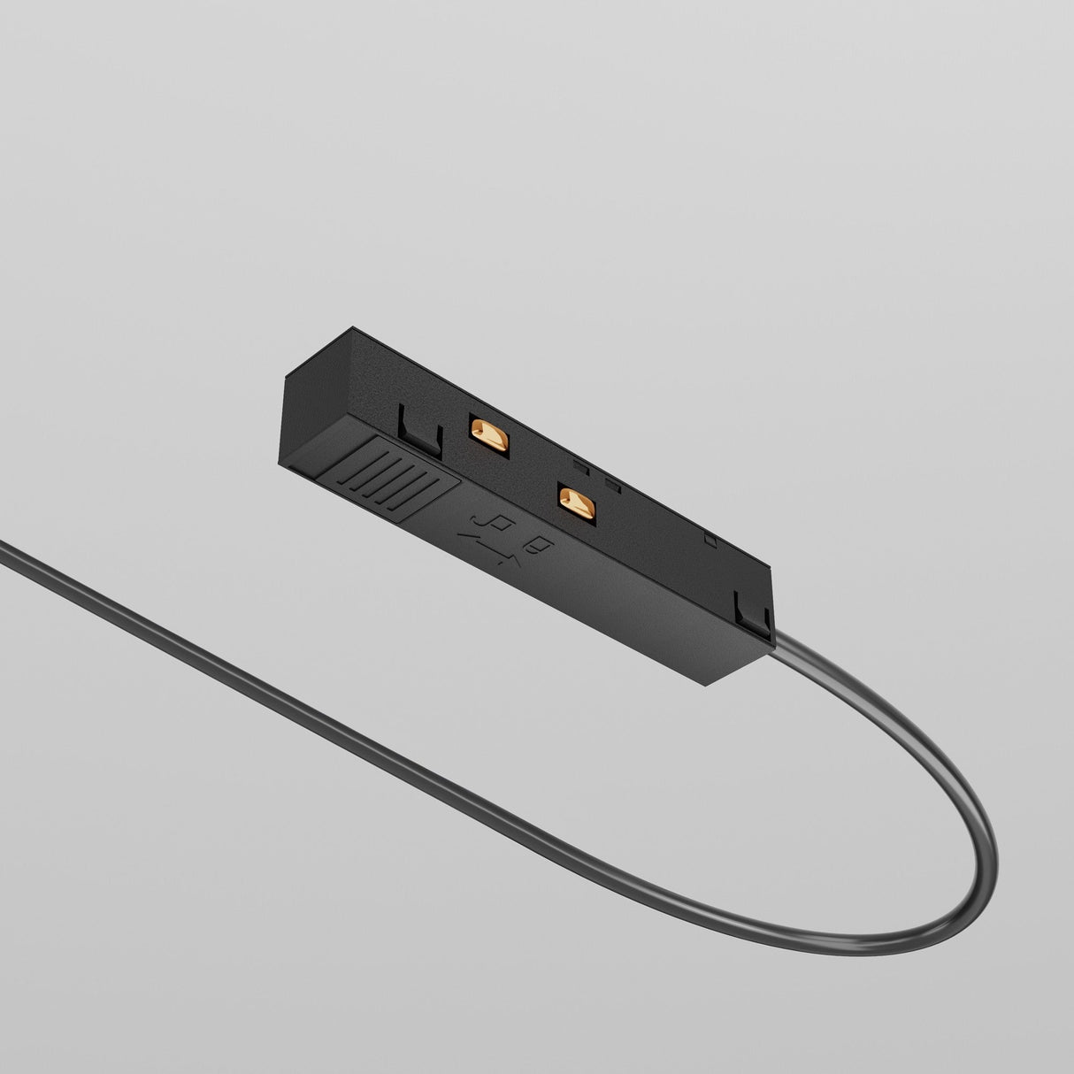 The Exility Track Power Feed - Black (TRA034B-42B) is a black, rectangular device with a cable and two gold connectors. It features small symbols on its surface and seamlessly integrates into a track lighting system against a plain gray background.