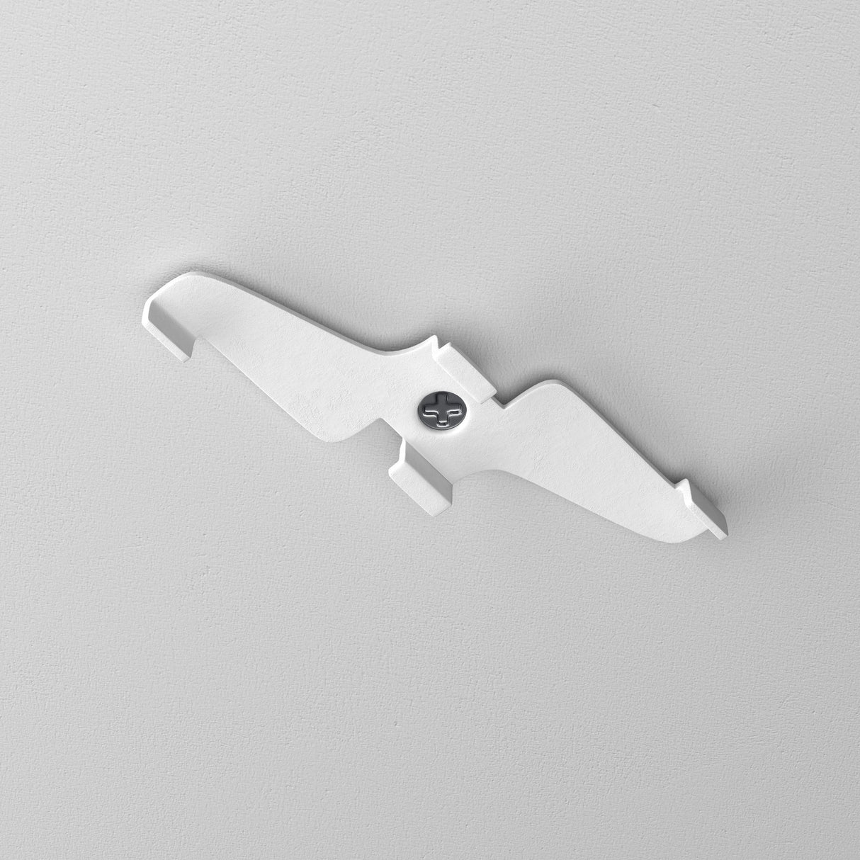 The Exility Magnetic Track Clamp - White creates a striking silhouette against the gray wall. Its minimalistic, bird-shaped design with outstretched wings harmonizes seamlessly with modern lighting, secured by a central screw for an elegant touch.