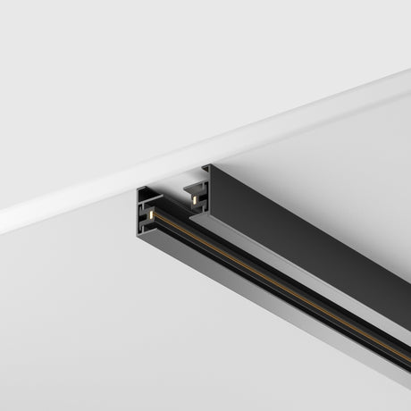 The Unity Single Phase Surface-Mounted Track 1m in black, with a sleek, minimalist design, is installed on a smooth white ceiling. Its single-phase system allows customizable lighting setups and highlights visible electrical connections for a modern touch.