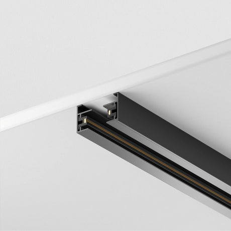 The Unity Single Phase Surface-Mounted Track 2m in black, crafted from aluminum, is seamlessly recessed into a white ceiling. It offers a sleek and modern design ideal for personalized lighting setups.