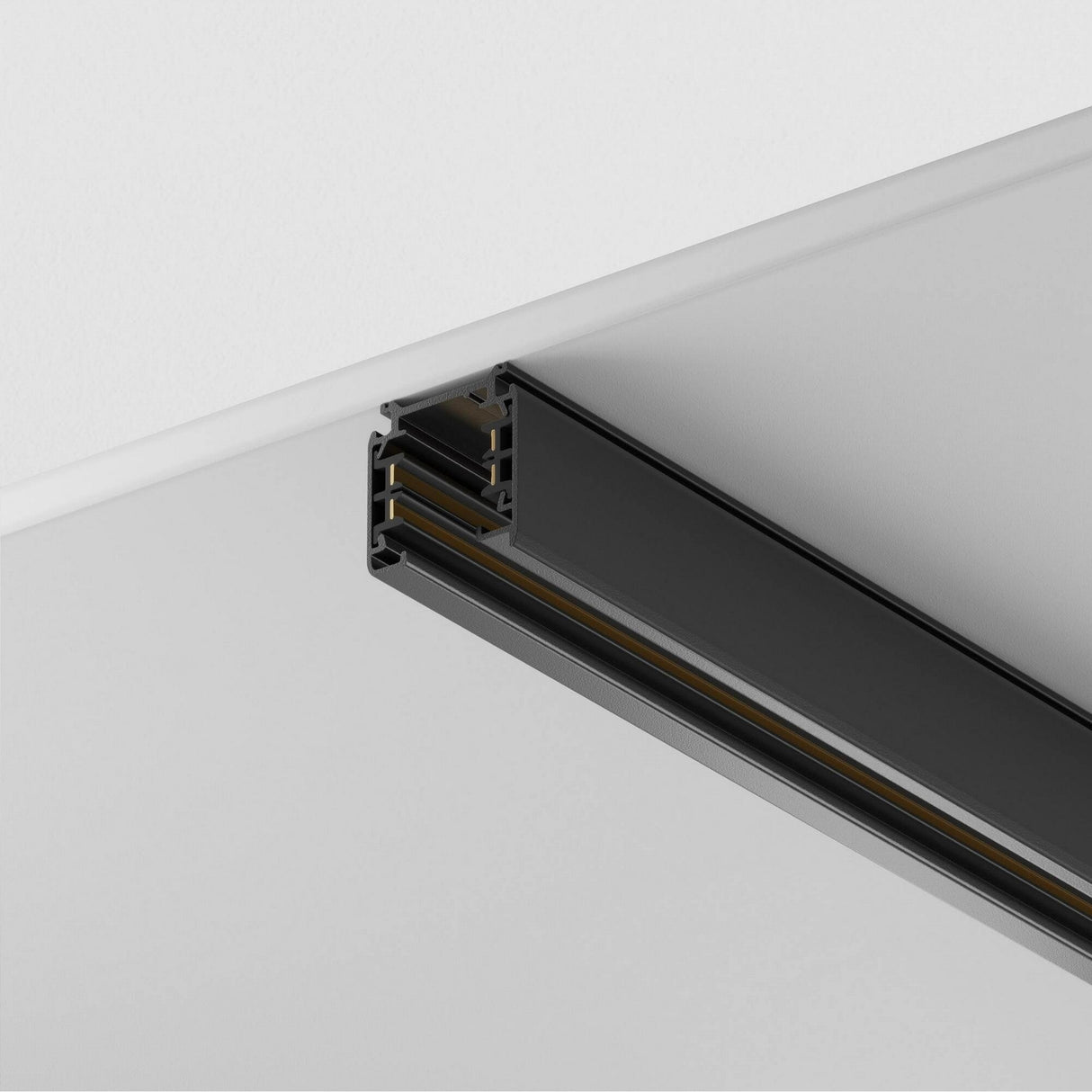 A close-up of the Trinity Three Phase Surface-Mounted Track 1m in black on a white ceiling showcases its sleek, minimalist design. Made from black aluminum, it emphasizes modern aesthetics with parallel lines and grooves, offering versatile ceiling lighting options.