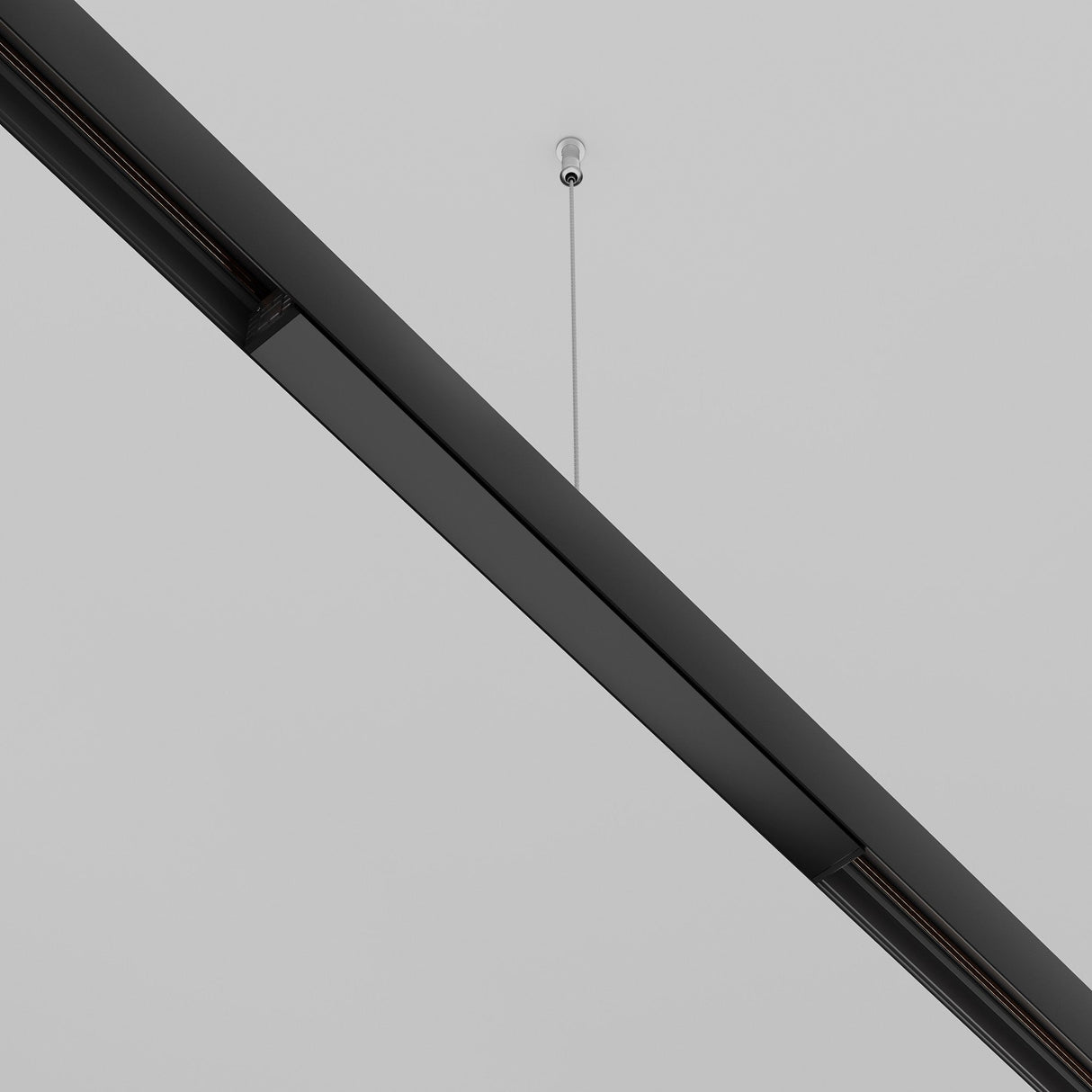 A sleek black linear light hangs from a white ceiling via a thin cable, exuding minimalist charm. Enhanced with the Exility Recessed Track Power Supply 100W - Black, it integrates seamlessly with recessed track lighting for optimal functionality.