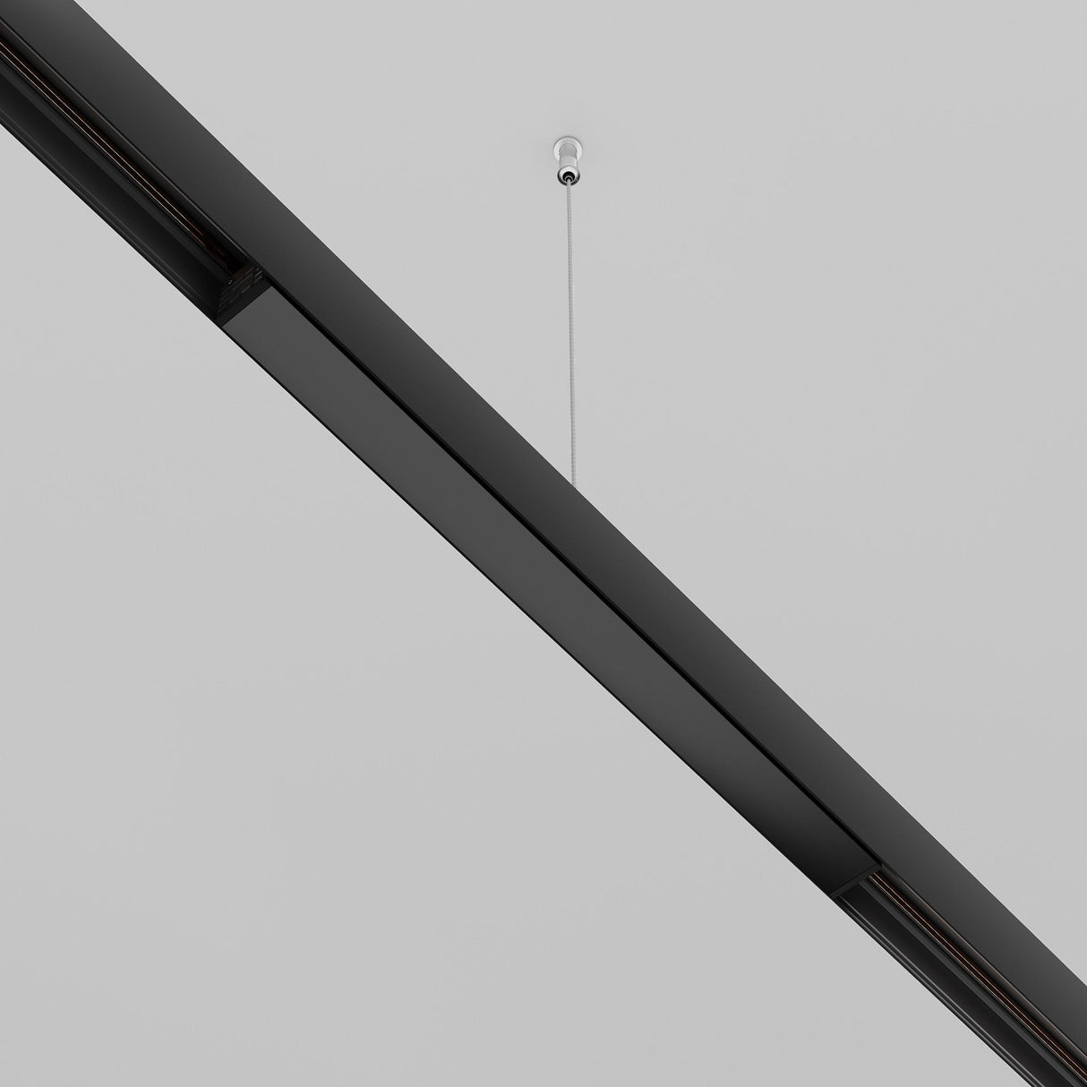 A close-up shows a minimalistic black linear light fixture hanging from a white ceiling by a thin wire. Enhanced by the Exility Recessed Track Power Supply 200W - Black, it exemplifies modern elegance and simplicity in recessed track lighting systems.
