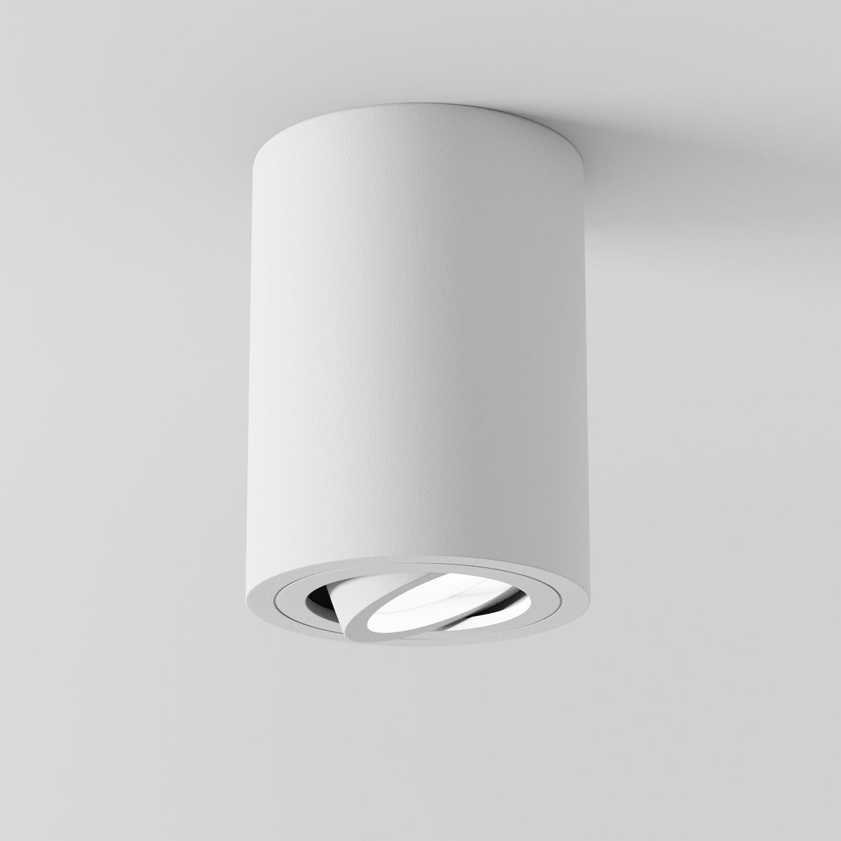 A sleek, modern white cylindrical ceiling light, the Atom Round Surface Mounted Downlight - White, is installed on a white ceiling. It features a recessed bulb and minimalist design with an elegant swivel function for perfect illumination.