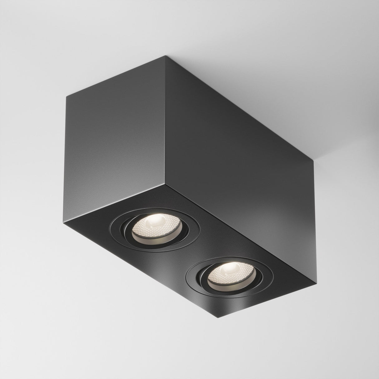 The Atom Twin Adjustable Rectangular Surface Mounted Downlight - Black features a dual light design with two circular LED lights. Its minimalist design contrasts strikingly against a white ceiling, exemplifying modern aesthetic lighting.