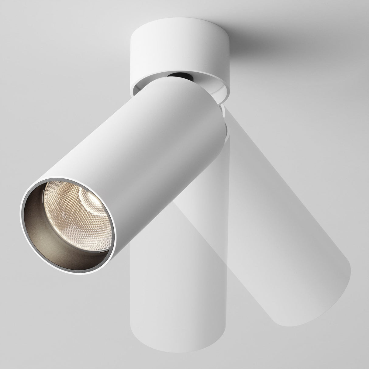 The Focus LED Single Surface-Mounted Spotlight 12W 3000K in white features a minimalistic design. Its adjustable cylindrical head directs light downward, creating subtle shadows on a light gray ceiling, offering modern and energy-efficient lighting.