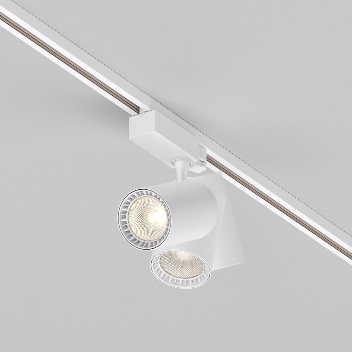 The Vuoro S 3-Circuit Trinity Track LED Spotlight 26W 3000K in white offers a sleek, modern look with dual adjustable spotlights. One spotlight shines brightly on a plain ceiling, enhancing the minimalistic design.