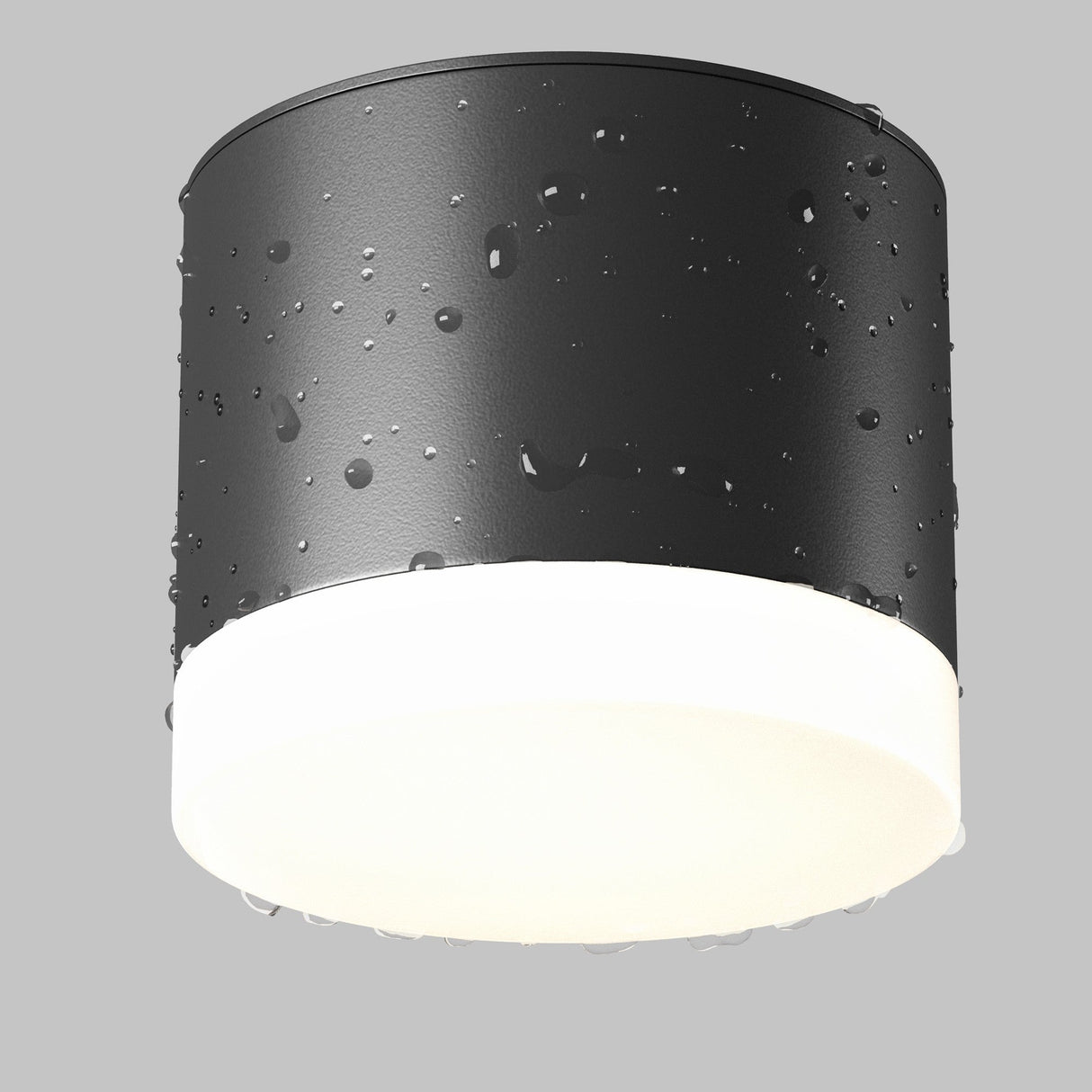 The Pauline Round Surface Downlight - Black, a cylindrical outdoor fixture, displays water droplets on its surface. It emits a soft white glow against a plain gray background, enhancing the scene with modern design elegance.
