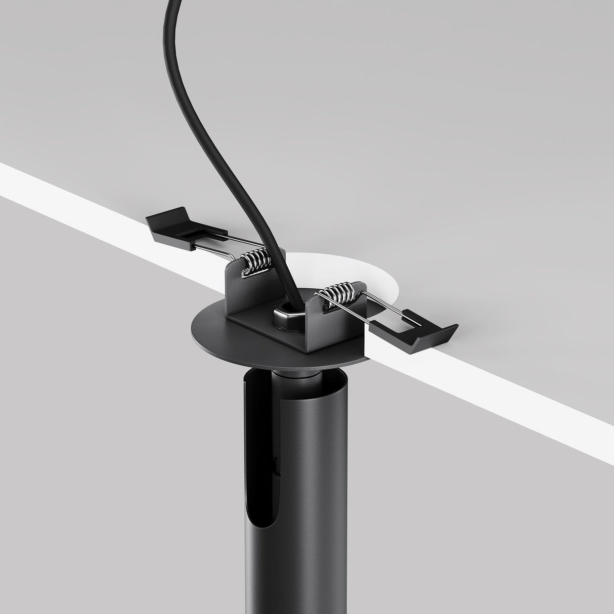 Close-up of a black Focus T LED Adjustable Long Recessed Downlight in a white desk, seamlessly fitting modern interiors. A cable threads through the grommet, secured underneath by two spring clamps. This setup organizes and guides cables neatly through the desktop.