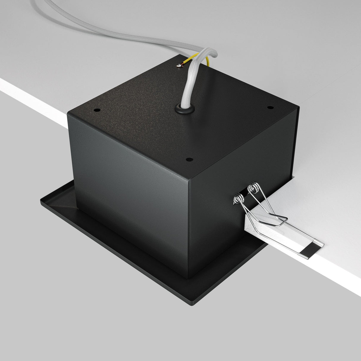 A Metal Modern Single Tilt Square Recessed Downlight in black, featuring a box design with wires on top, is mounted on a flat surface for seamless integration with recessed lighting; a binder clip attached holds a white label.